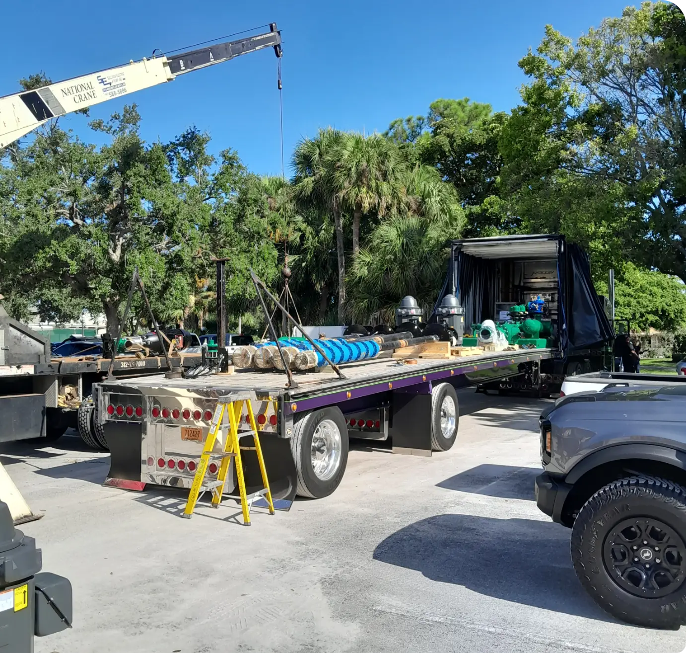 Knuckle-boom crane unloading well pump piping from flatbed truck