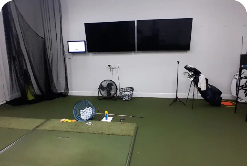 Dual-screen indoor golf practice room with hitting mats and clubs