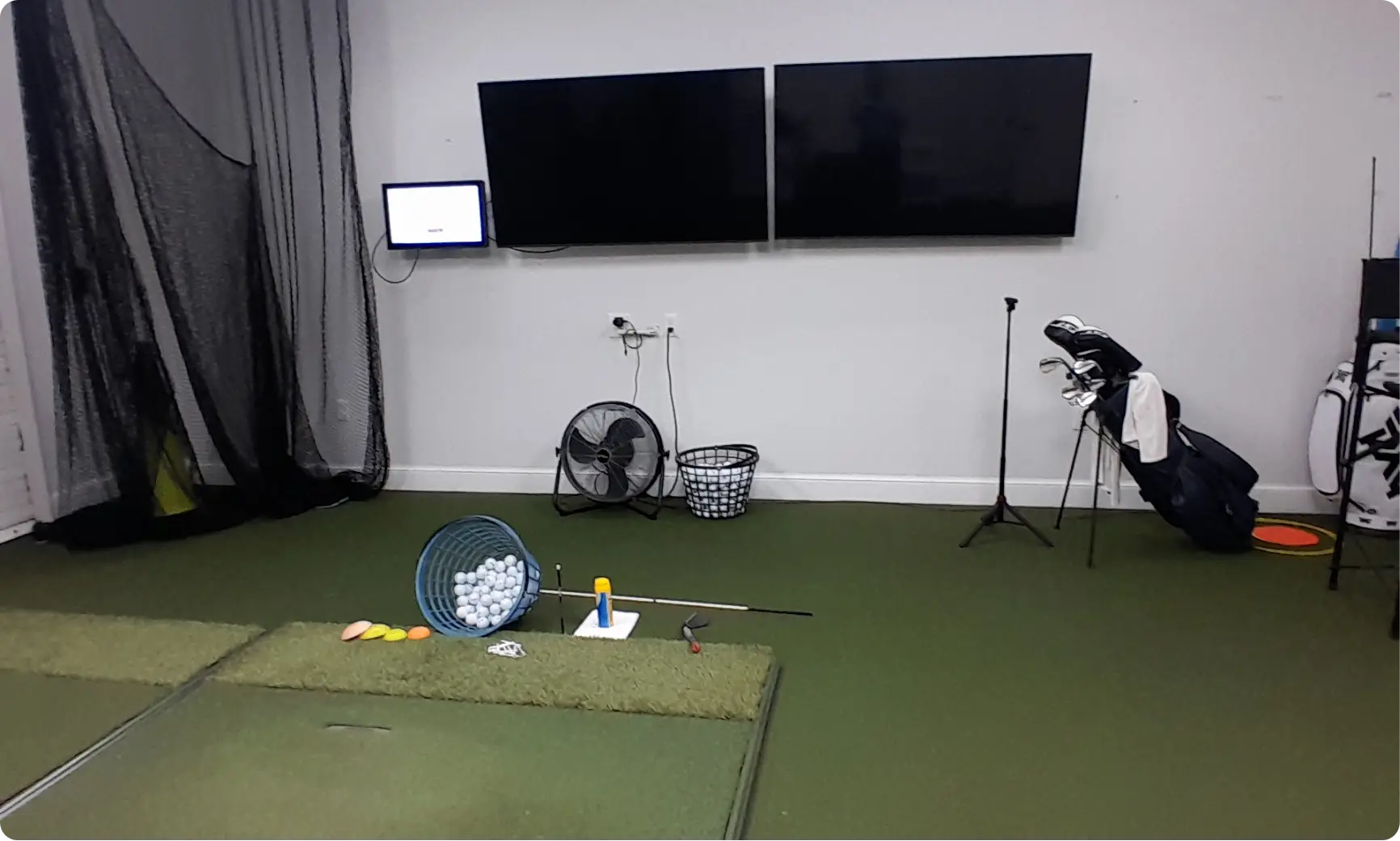 Indoor golf simulator bay with hitting mats, screens, and club bag