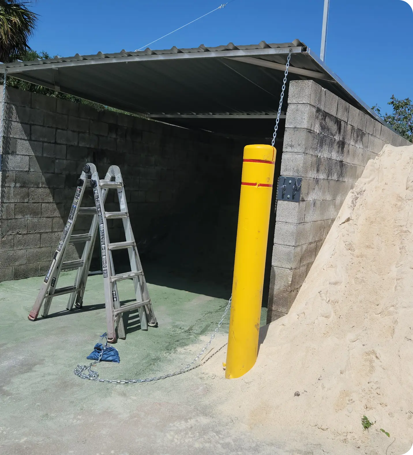Concrete-block soil bin bay with steel roof and yellow bollard