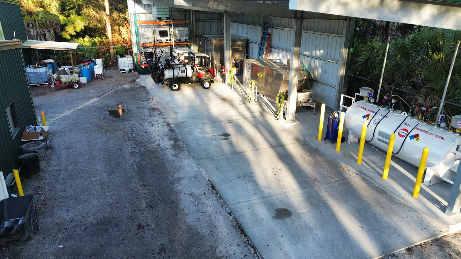 Aerial view of the Naples Heritage fuel area showing the pitched concrete pad, bollard-protected fuel tank, and covered mix load station.