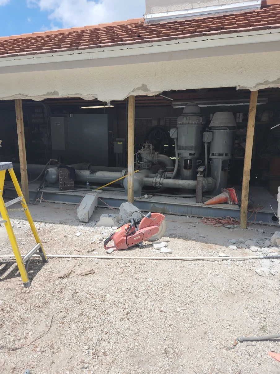 The Naples Heritage pump house with a section of block wall removed and shoring posts in place, exposing the old irrigation pump station inside for removal.