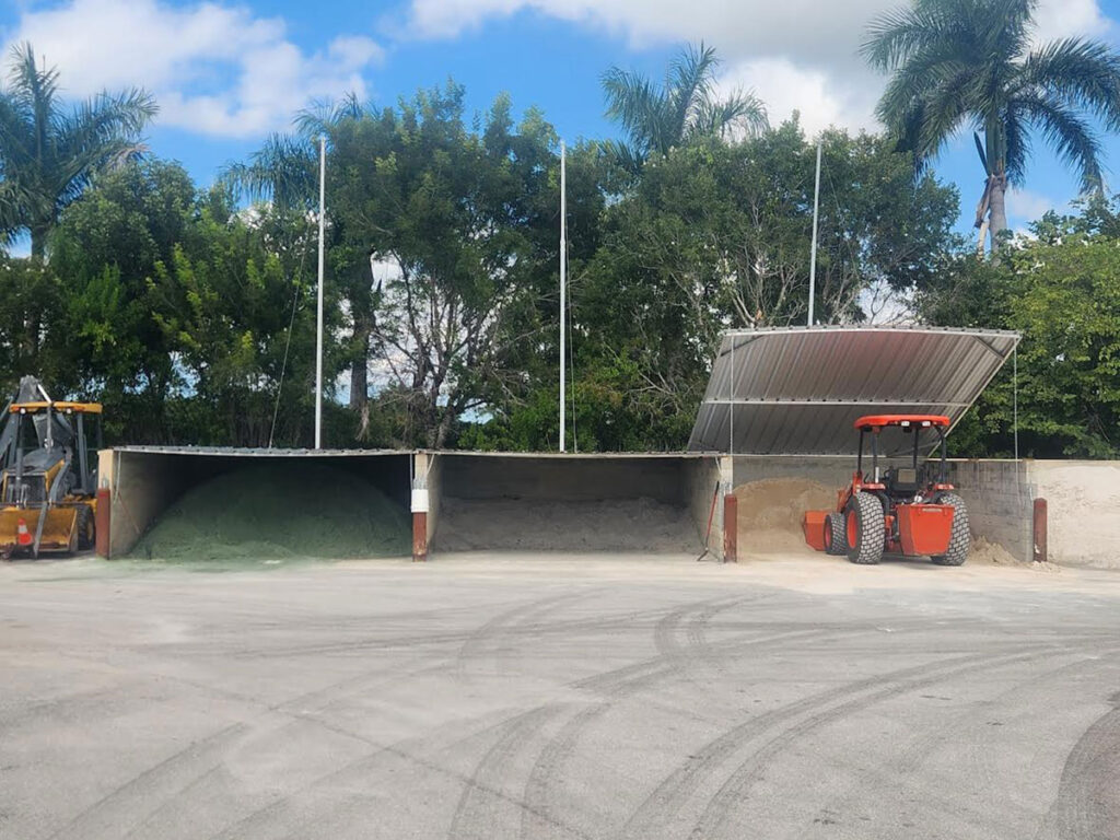 Three-bay soil bin covers with steel lift-up lids open, storing green topdressing and sand at a golf course maintenance facility