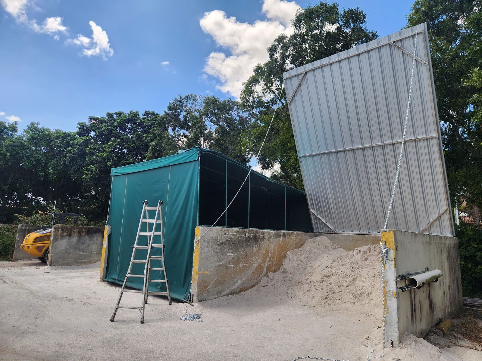 Soil bin cover with green canvas siding and steel lift-up roof storing sand at a golf course maintenance facility