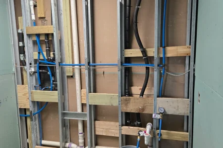 Stud wall with blue PEX and black drain plumbing rough-in