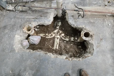Broken-out concrete floor exposing old drain piping