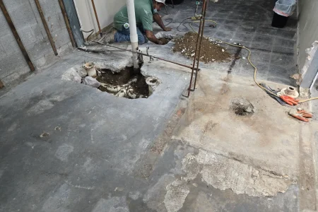 Worker repiping plumbing in opened concrete floor trench