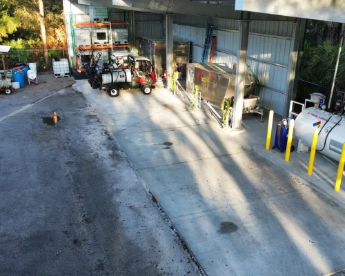 Aerial view of the Naples Heritage fuel area showing the pitched concrete pad, bollard-protected fuel tank, and covered mix load station.