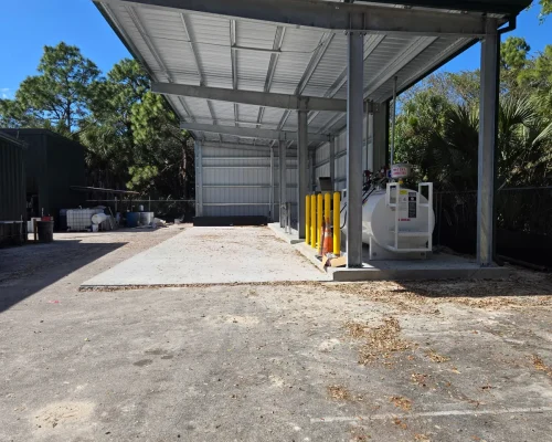 Side view of the finished Naples Heritage canopy with green roofline and a bollard-protected fuel tank under clear blue sky.