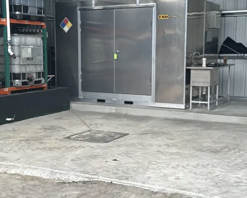 Stainless mix and wash enclosure at Naples Heritage beside the tote rack, with a relocated sump set into the pitched concrete out of the drive path.
