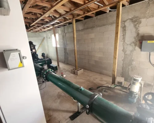 Interior of the Naples Heritage pump house showing the new irrigation pump station with its control cabinet and green discharge piping installed and operational.