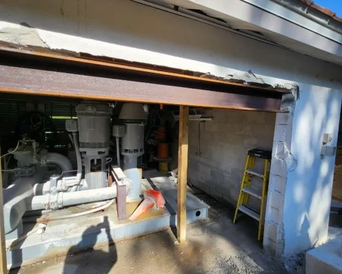 The new irrigation pump station set in place inside the Naples Heritage pump house, with the structural header beam overhead and block wall rebuild beginning.
