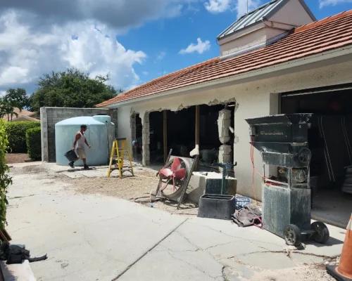 Wide exterior view of the Naples Heritage pump house during the wall opening, with the work zone, water tank, and staging equipment around the building.