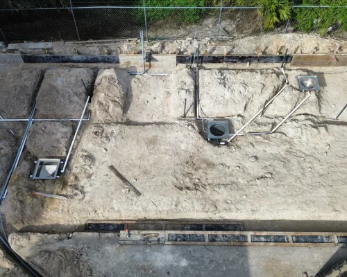 Early construction view of the Naples Heritage site showing underground drain lines, sumps, and plumbing rough-in before the concrete pour.