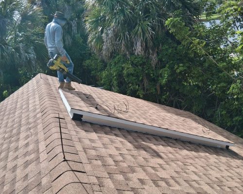 The finished hip roof on the Old Marsh pump house, fully reshingled, as a Roughneck Ranch crew member clears debris from the new surface