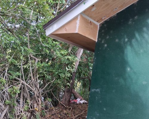 New plywood soffit and white fascia trim installed at the eave of the Old Marsh pump house, replacing the previously rotted woodwork