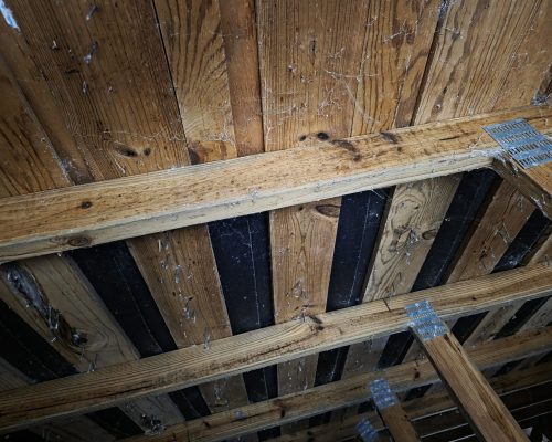 Close view of the Old Marsh pump house roof structure before repair, with water-stained and rotted roof sheathing between aging trusses joined by metal gusset plates