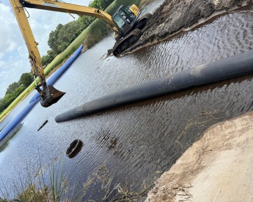 Installation of the new flume pipe at Pine Tree Golf Club, with the HDPE pipe floated into position across the pond and a dewatering dam holding back the water