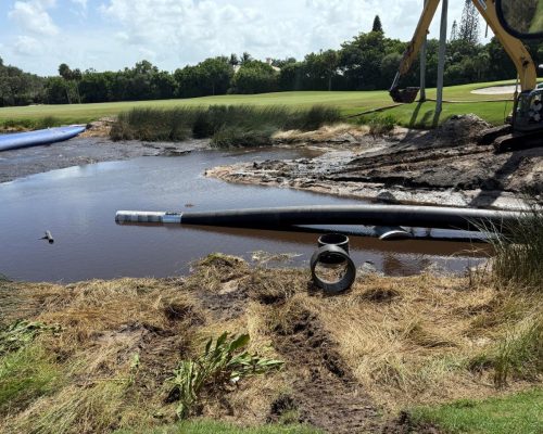 Large HDPE flume intake pipe installed running out into the irrigation lake at Pine Tree Golf Club, with a screened intake end and an excavator alongside