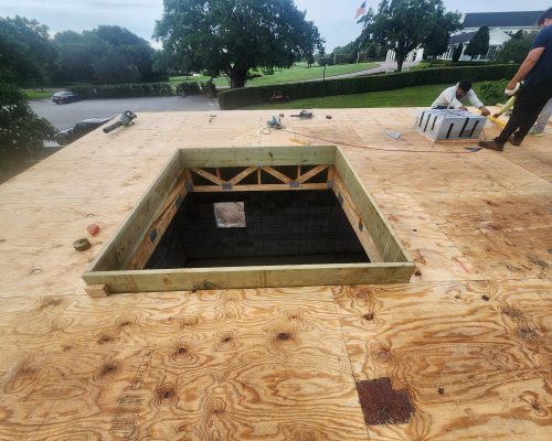 Construction of the Pine Tree Golf Club pumphouse, looking down through the roof opening into the block-walled pump room as the crew sheathes the roof, with the clubhouse in the background