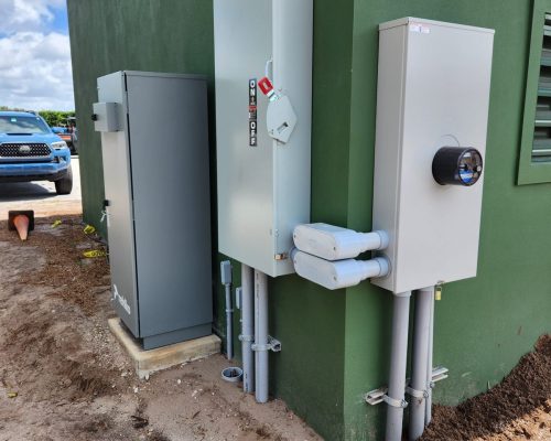 Electrical service for the completed Pine Tree pumphouse, with a disconnect, panel, and meter mounted on the green stucco wall feeding the irrigation pump system