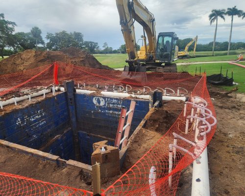 Excavation of the new wet well at Pine Tree Golf Club, with trench-box shoring in place and irrigation mains being routed alongside an excavator on the course
